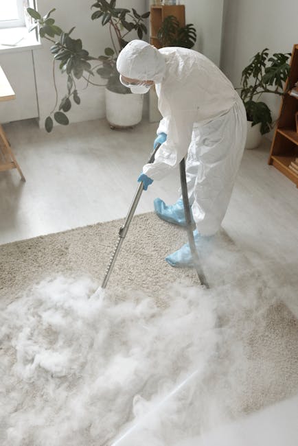 A professional cleaner from Carpet Cleaners W14 wearing a white protective suit, mask, and gloves is performing deep carpet cleaning in a bright, modern living room. The cleaner is using a steam clean