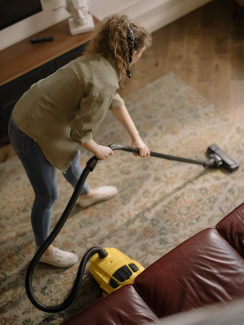 A professional cleaner from Carpet Cleaners W14 wearing a white protective suit, mask, and gloves is performing deep carpet cleaning in a bright, modern living room. The cleaner is using a steam clean