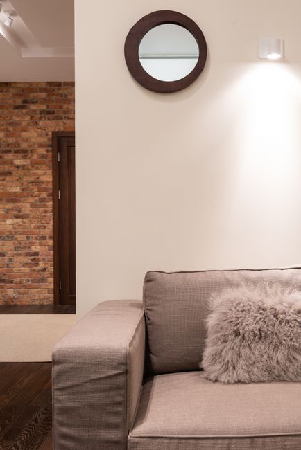 A cozy living room corner featuring a plush, dark-colored sofa adorned with patterned cushions, situated next to a window with partially pulled curtains allowing natural light to softly illuminate the